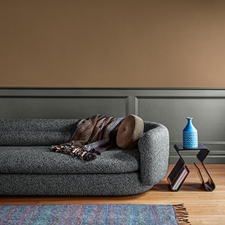 A oblong gray couch topped with a throw pillow and blanket sit near a colorful accent rug in a minimalist living room.